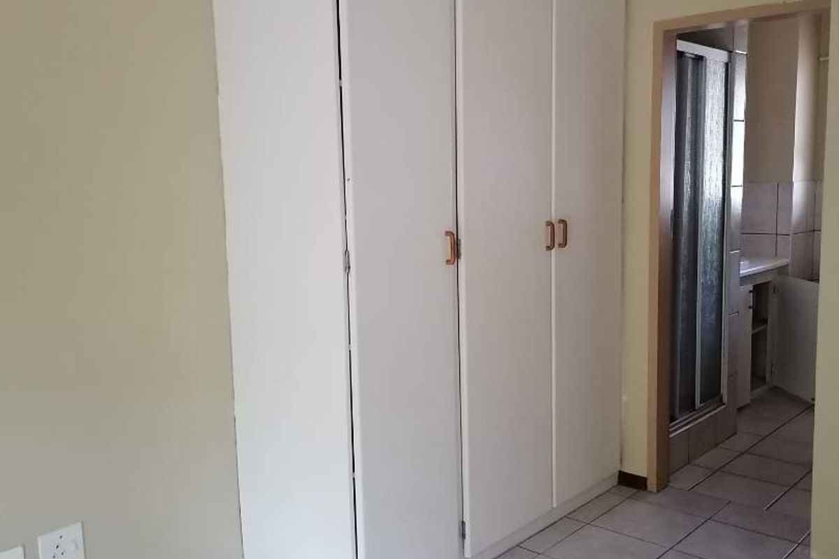 A simple bedroom featuring tiled flooring and a built-in wardrobe, with direct access to an adjacent bathroom area.