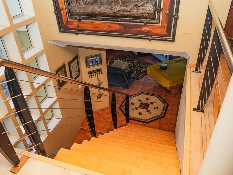 A staircase with timber treads and a modern metal balustrade leading down to a tiled lower level with large windows.