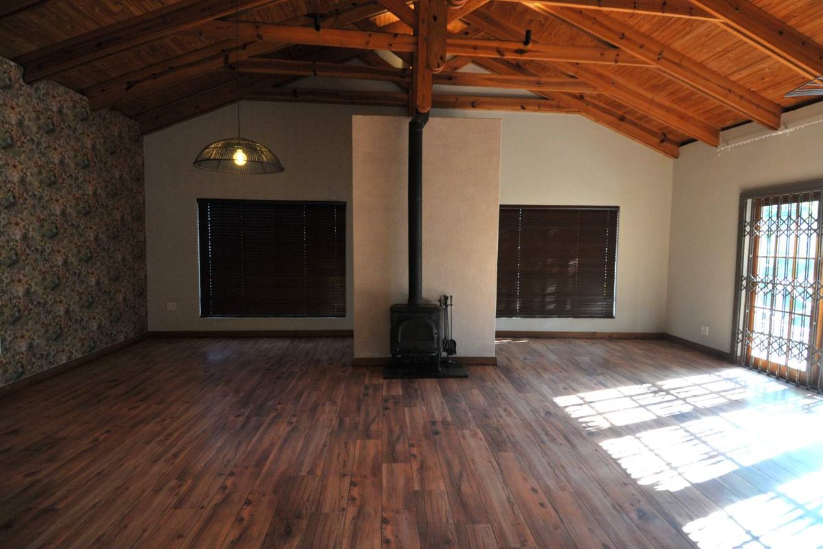 Spacious living area featuring high vaulted timber ceilings, wood-burning fireplace, and durable wood-look flooring with access to an outdoor area.
