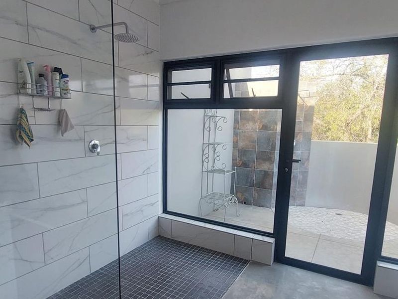Modern bathroom featuring a spacious walk-in shower with marble-look tiling, a rain shower head, and large aluminium-framed windows providing natural light and outdoor access.