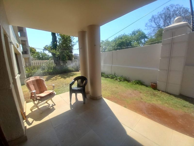 A covered patio area featuring tiled flooring and structural columns, overlooking a private garden space enclosed by a perimeter boundary wall.