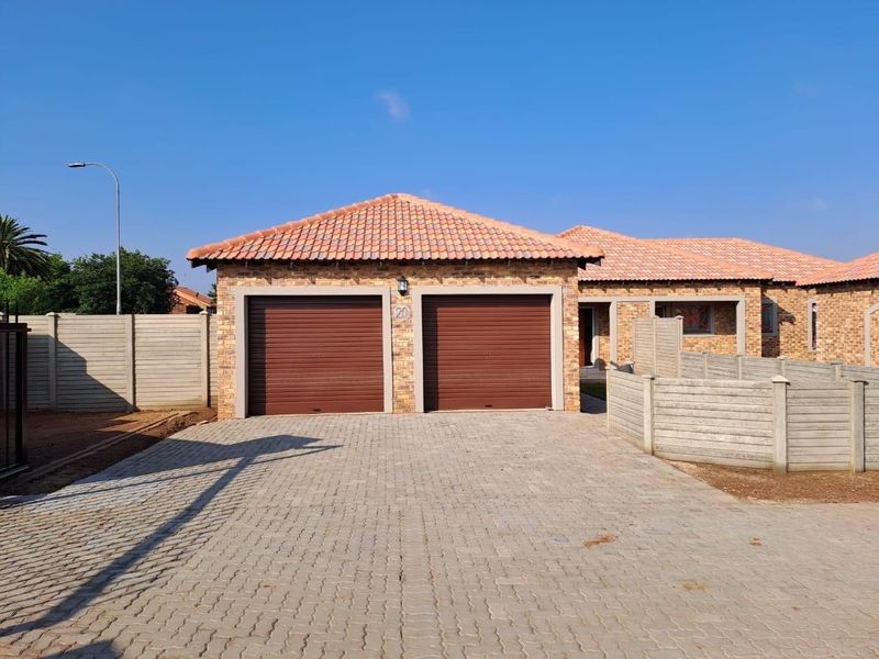Front view of a townhouse featuring a double garage with roller doors, a paved driveway, and a brick facade with a tiled roof.