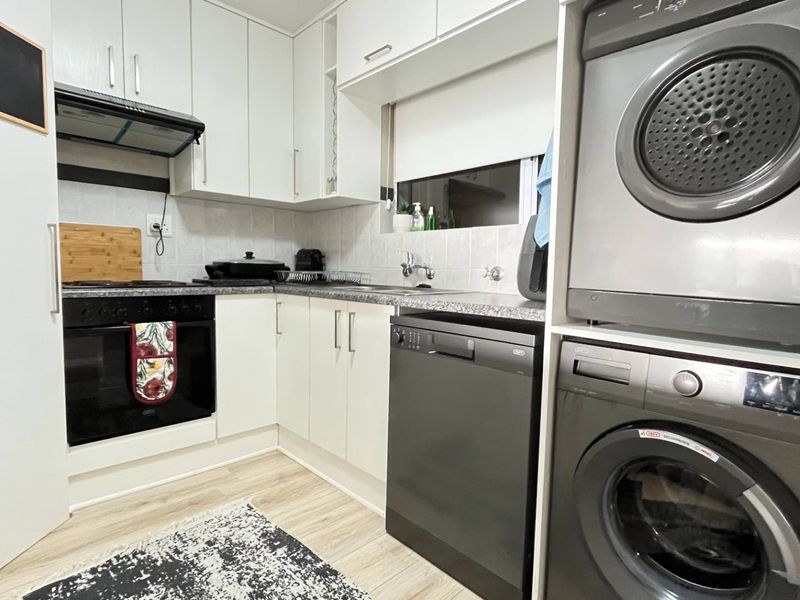 Modern kitchen featuring white cabinetry, granite countertops, integrated oven, extractor fan, dishwasher, and a convenient stacked laundry area.