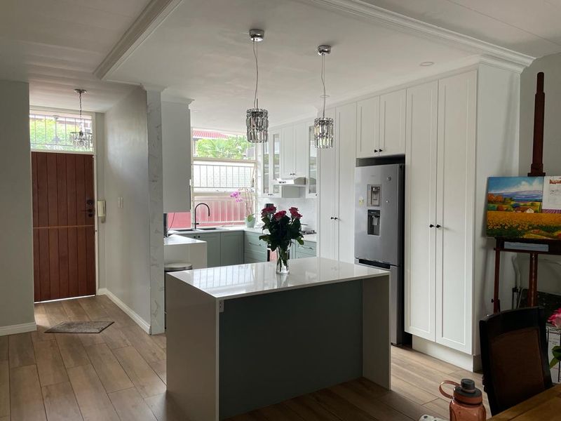 Modern kitchen featuring a central island, sleek white cabinetry, quartz countertops, and contemporary pendant lighting, seamlessly integrated into an open-plan living space.