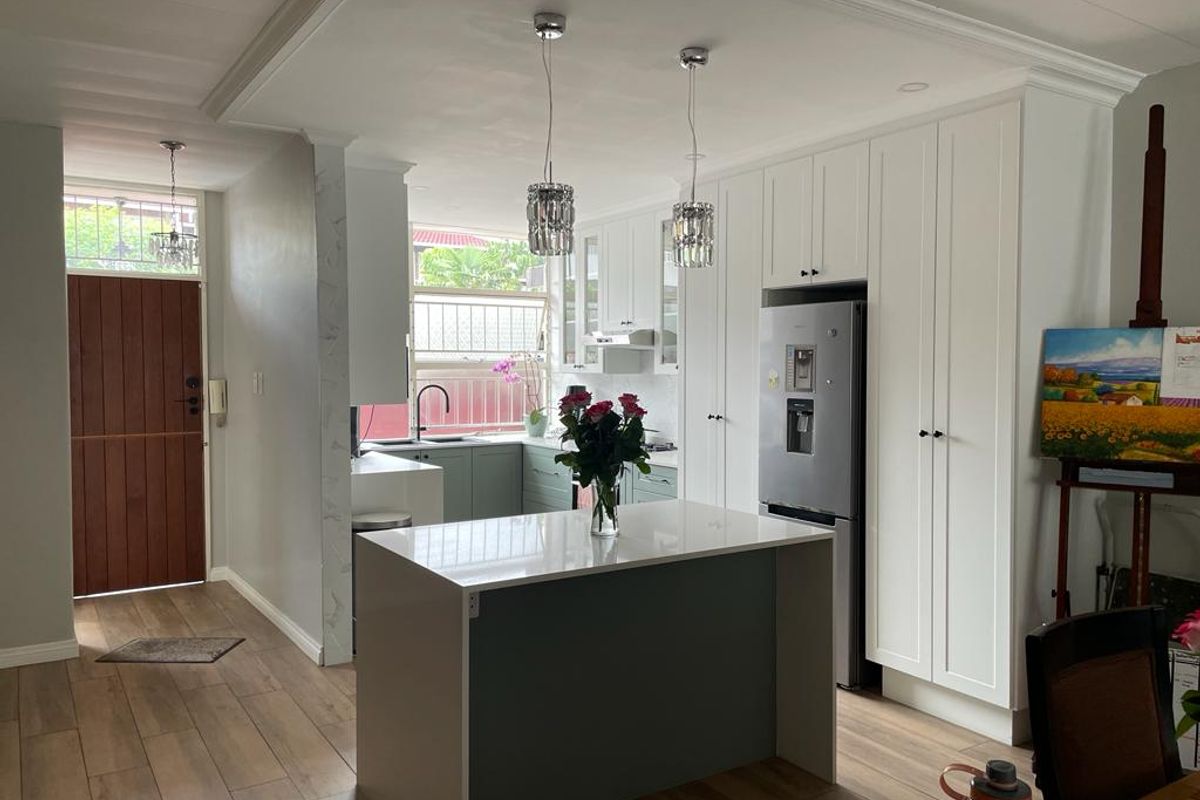 Modern kitchen featuring a central island, sleek white cabinetry, quartz countertops, and contemporary pendant lighting, seamlessly integrated into an open-plan living space.