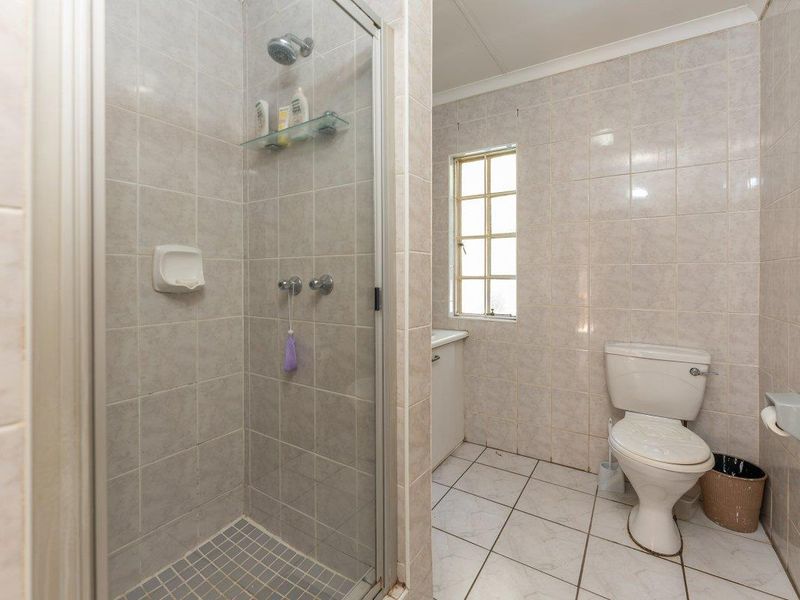 A functional bathroom featuring a glass-enclosed shower, tiled walls and flooring, a standard toilet, and a small vanity cabinet.
