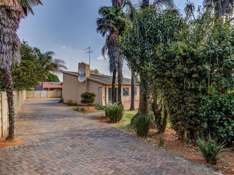 A view of the property's paved driveway leading to the front entrance, featuring established trees and a secure boundary wall.
