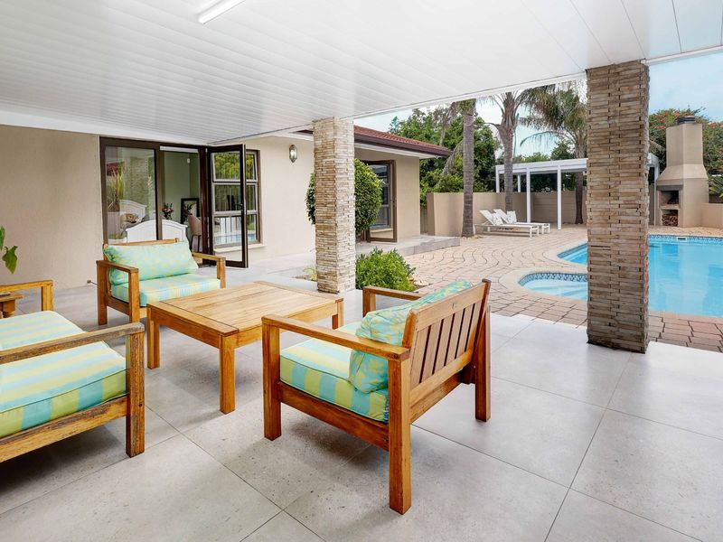Spacious covered patio featuring stone-clad columns, overlooking a well-maintained swimming pool area with an outdoor fireplace and paved deck.
