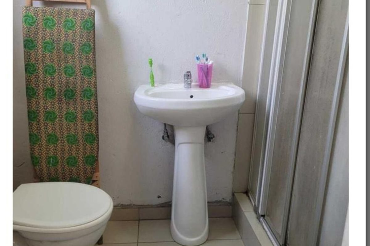 A compact bathroom featuring a pedestal basin, toilet, and shower enclosure with tiled flooring and basic wall finishes.