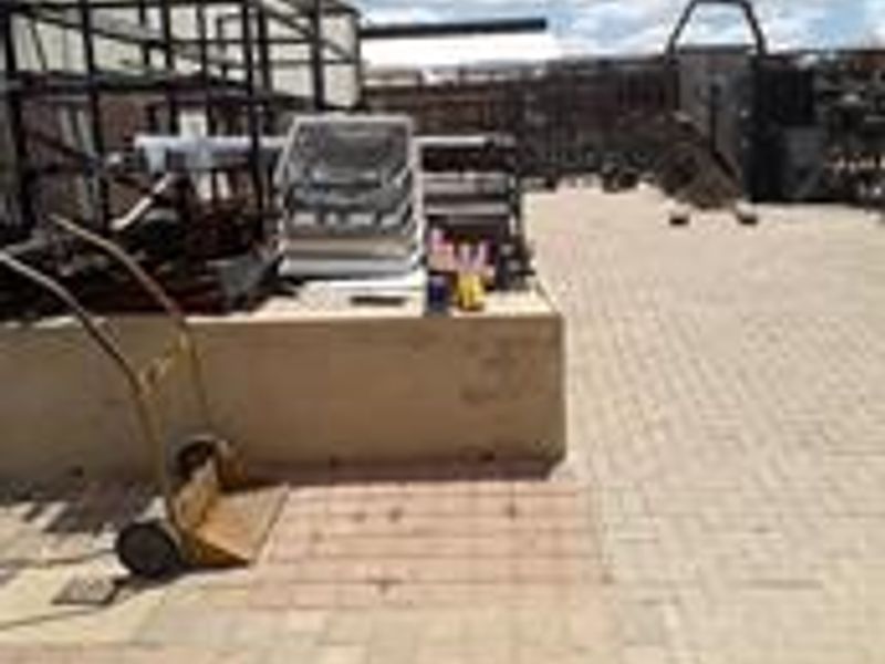 An industrial rear yard area featuring paved ground surfaces, a low retaining wall, and fixed metal racking structures.