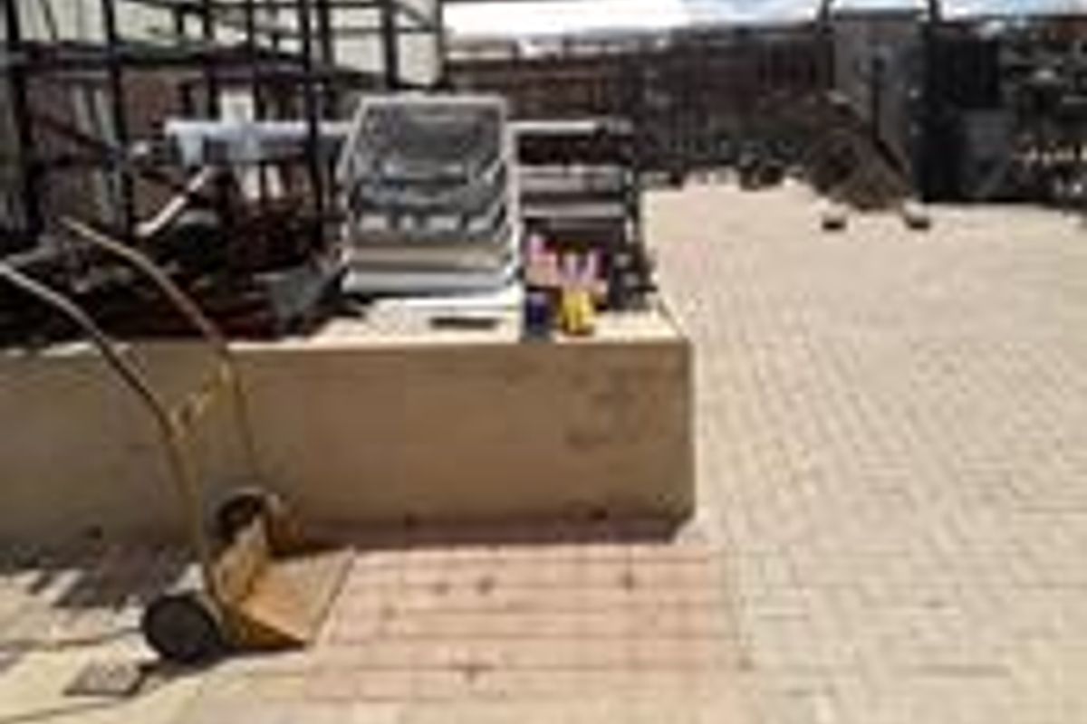 An industrial rear yard area featuring paved ground surfaces, a low retaining wall, and fixed metal racking structures.
