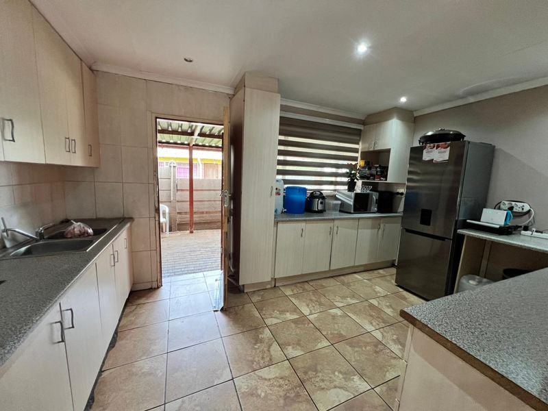 Functional kitchen featuring built-in cabinetry, laminate countertops, double bowl sink, and tiled flooring with direct access to an outdoor patio area.