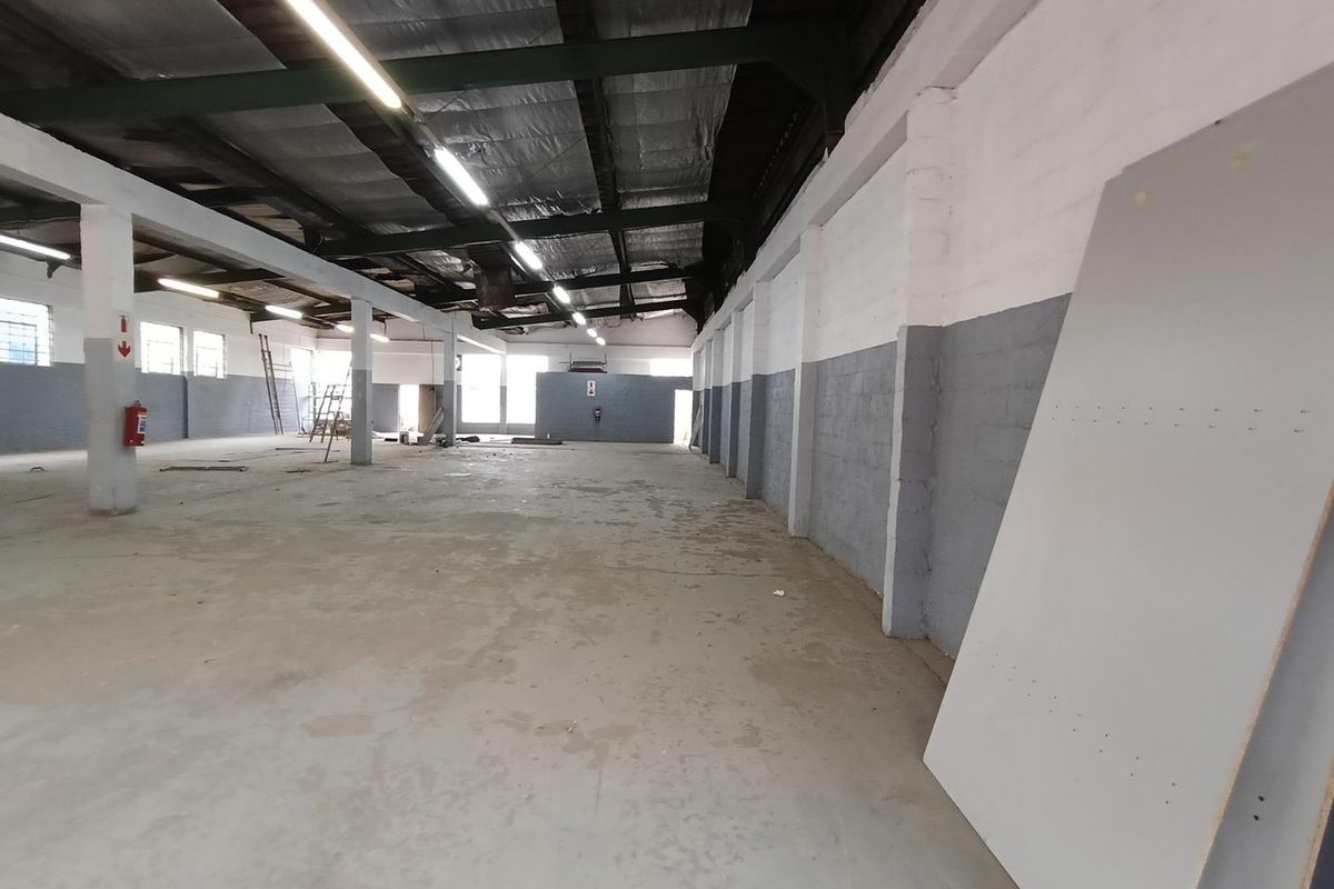 Spacious industrial warehouse unit featuring high exposed ceilings, concrete flooring, and functional strip lighting, suitable for storage or light manufacturing operations.
