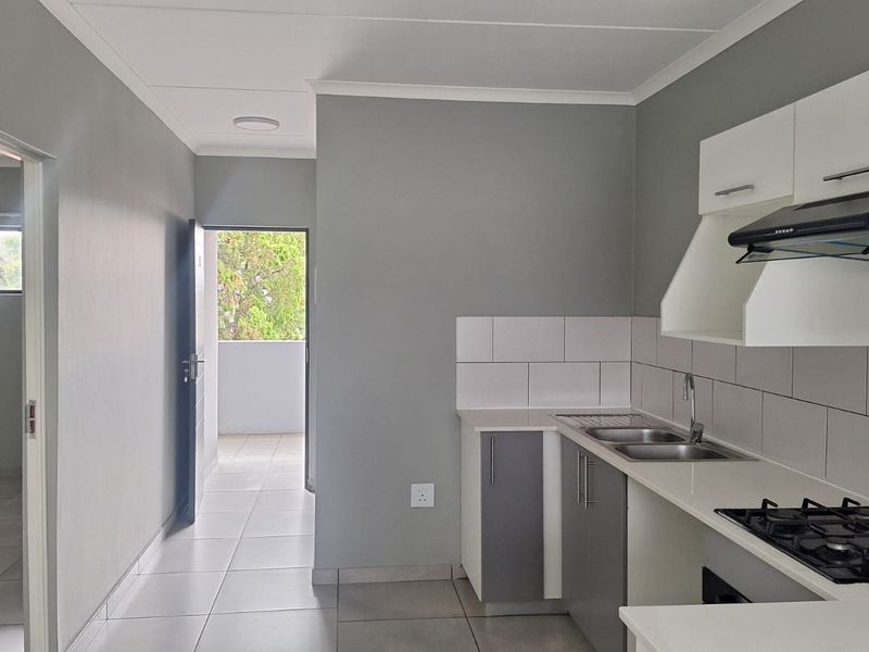 Modern kitchen featuring built-in cabinetry, gas hob, extractor fan, and tiled splashback, leading to an open hallway and balcony area.