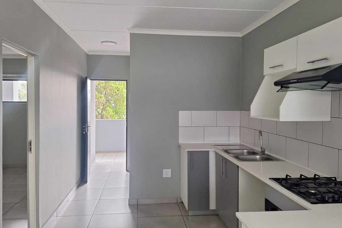 Modern kitchen featuring built-in cabinetry, gas hob, extractor fan, and tiled splashback, leading to an open hallway and balcony area.