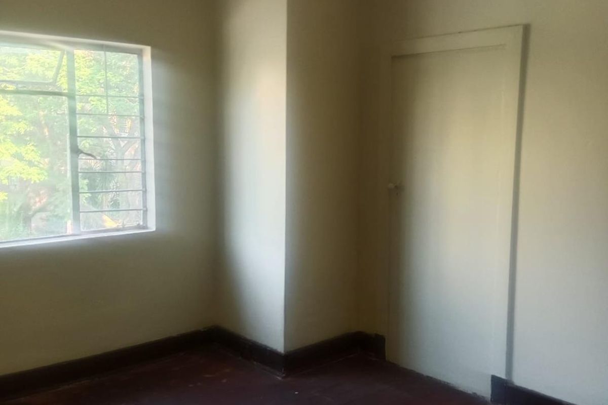 A vacant bedroom featuring original timber flooring, a single window with security bars, and a classic interior door.