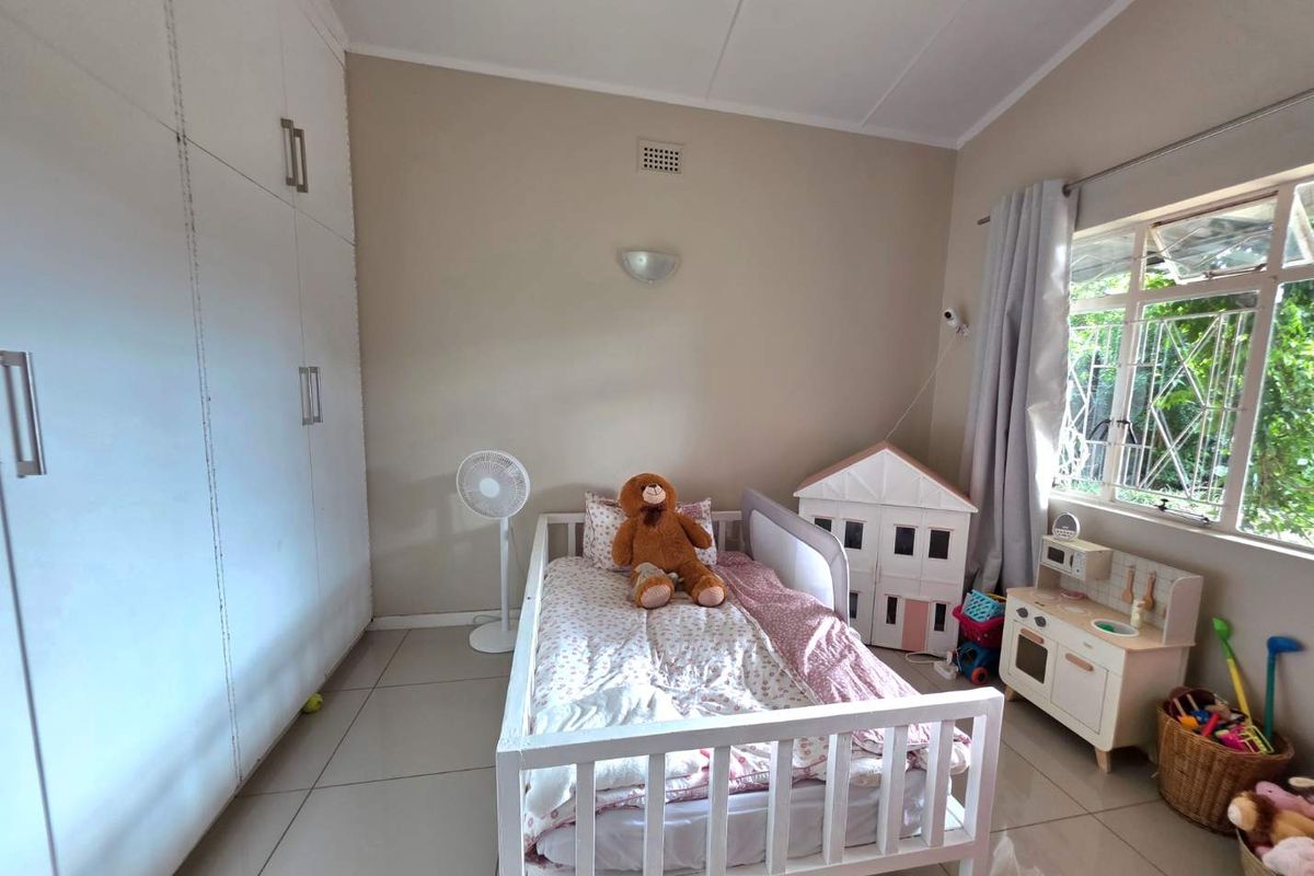 A bedroom featuring built-in cupboards, tiled flooring, and a window with security bars, providing a functional and well-lit living space.