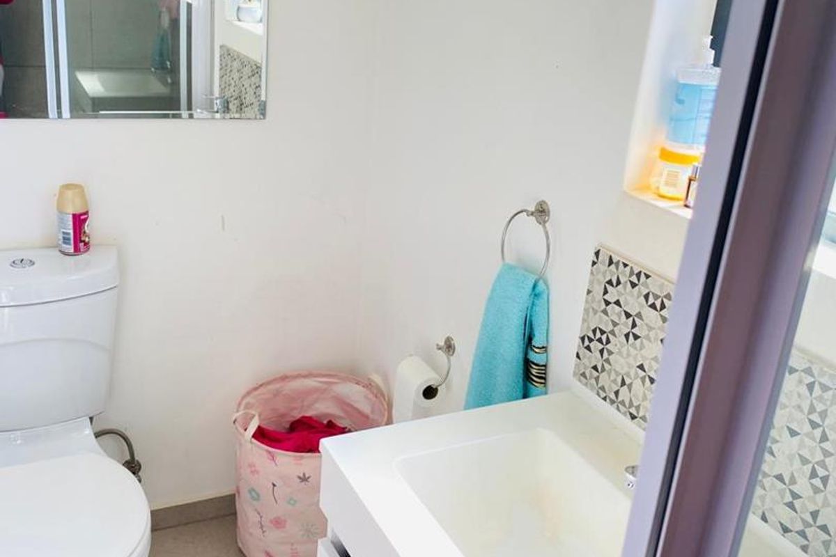 A functional bathroom featuring a modern white vanity cabinet, ceramic basin, toilet, and decorative tiled splashback with neutral floor tiles.