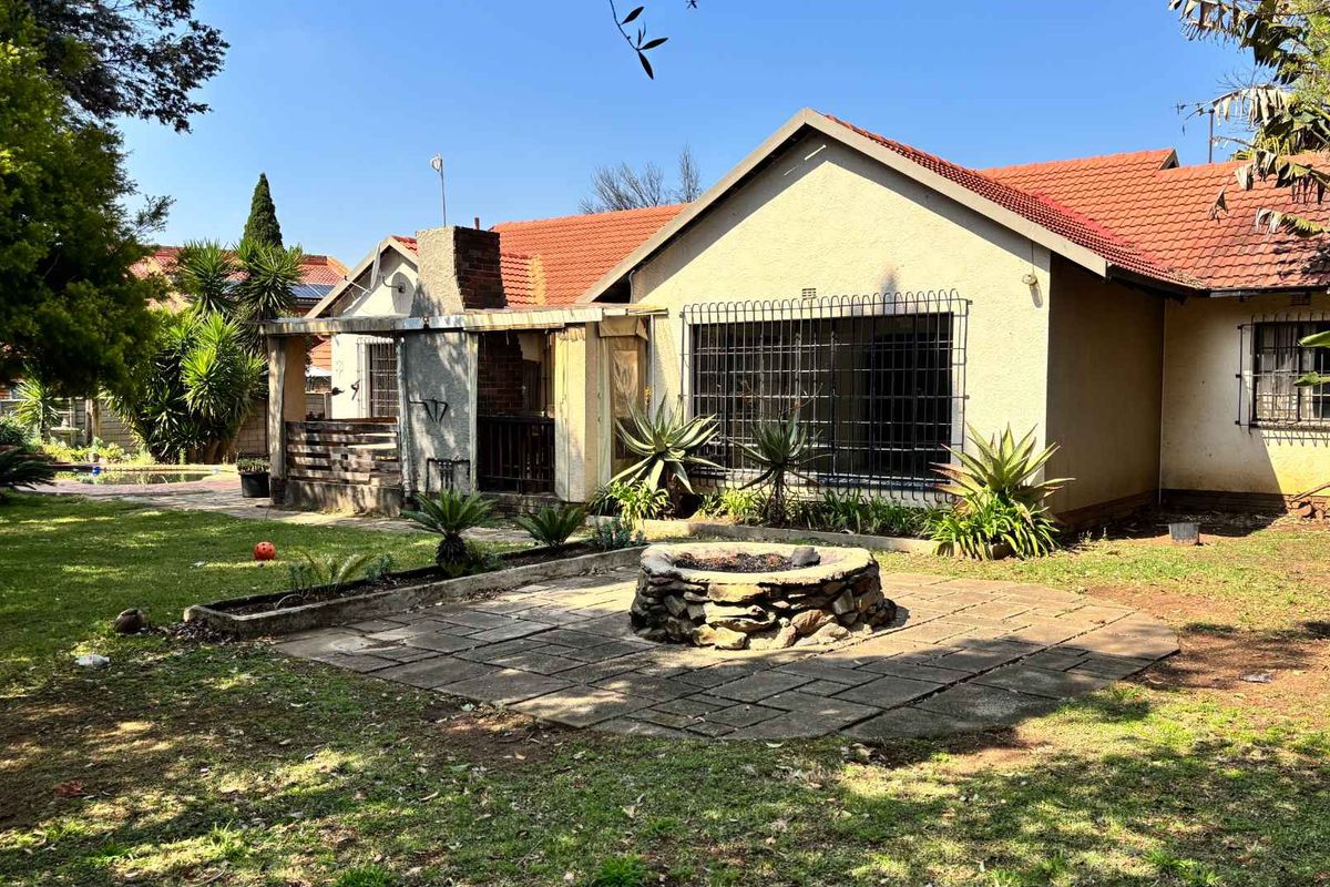 Rear view of the house featuring a paved patio area with a stone fire pit, tiled roof, and established garden surroundings.