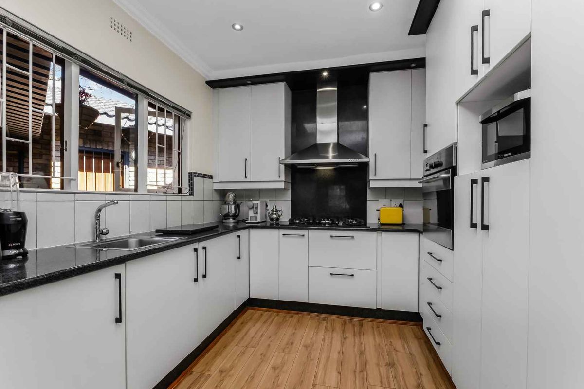Modern kitchen featuring white cabinetry, granite countertops, stainless steel appliances, gas hob, and integrated oven with wood-look laminate flooring.