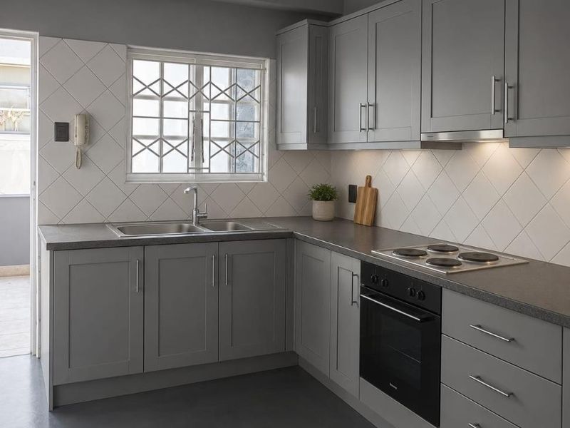 Modern kitchen featuring grey shaker-style cabinetry, integrated electric oven and hob, diamond-patterned wall tiles, and a functional layout with ample storage.