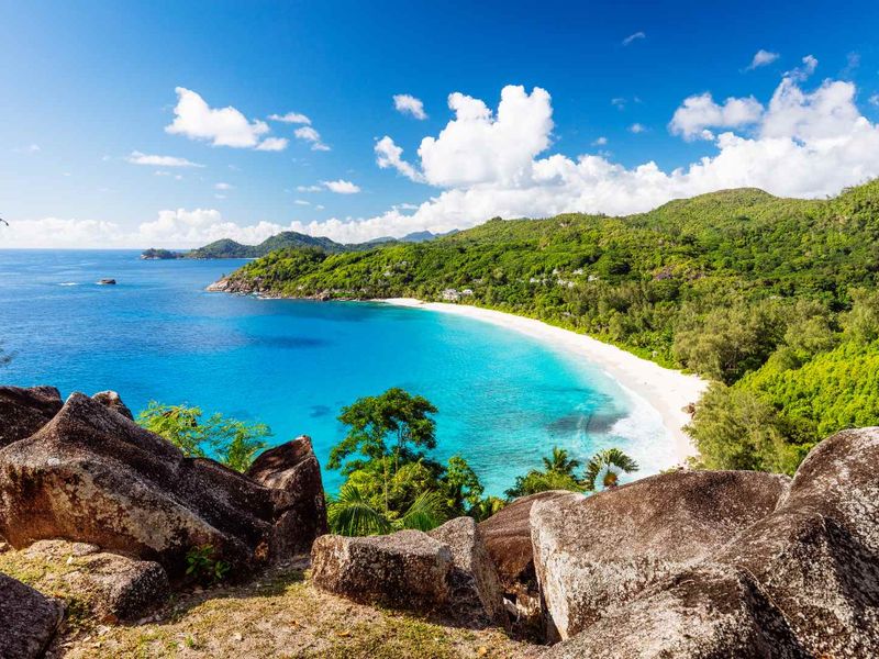 A scenic elevated view overlooking a pristine tropical beach with turquoise waters, white sand, and lush green coastal vegetation.
