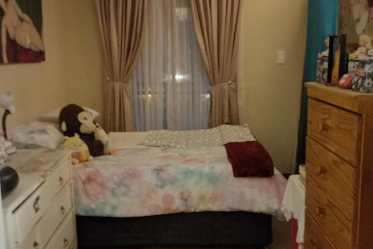 A cozy bedroom featuring neutral wall tones, carpeted flooring, and a window dressed with curtains, providing a functional and comfortable living space.