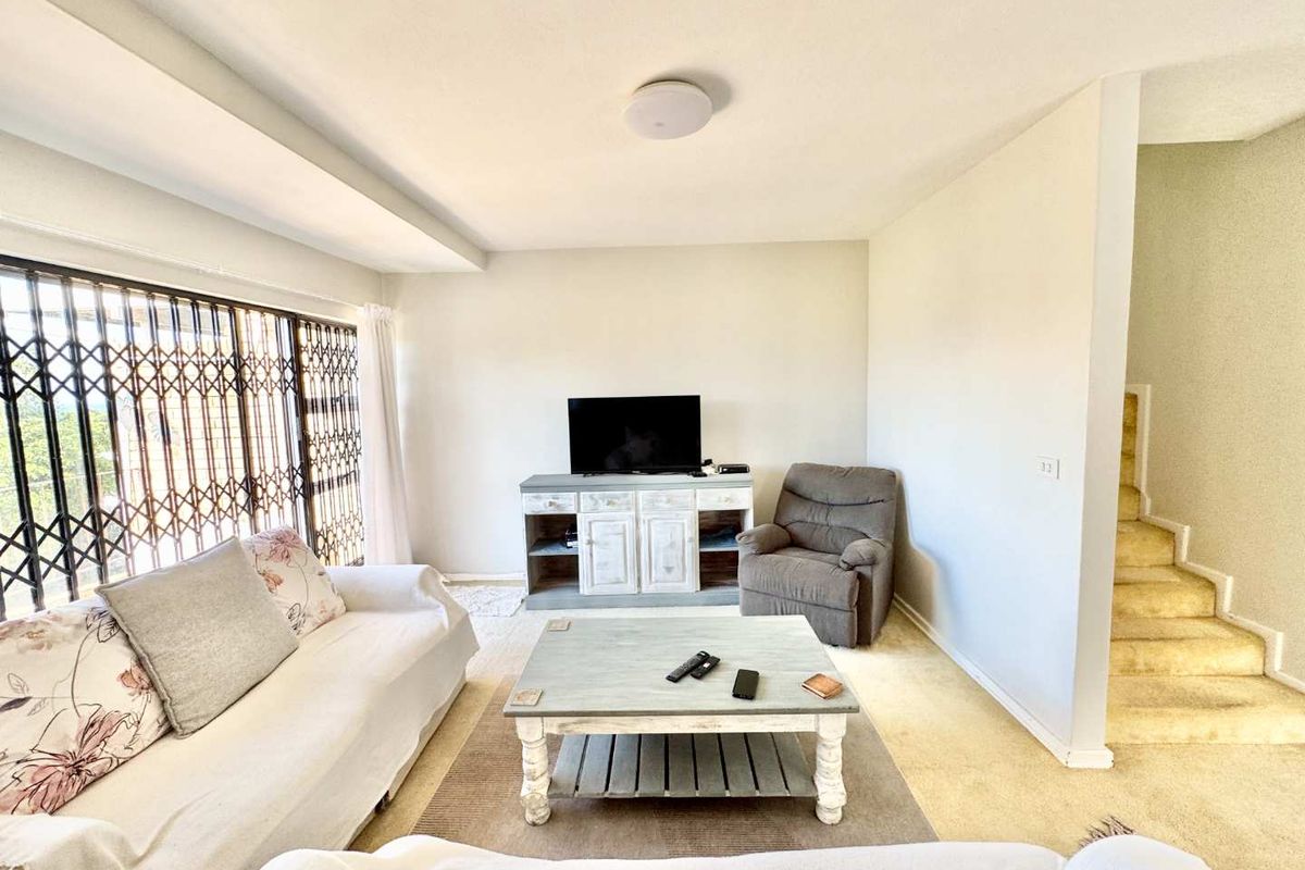 A living room featuring carpeted flooring, a staircase, and a large window with a security gate.