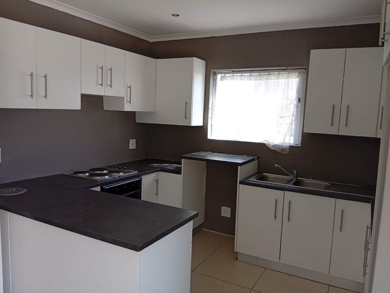 A functional kitchen featuring white cabinetry, dark countertops, a built-in oven and hob, and a double stainless steel sink with tiled flooring.