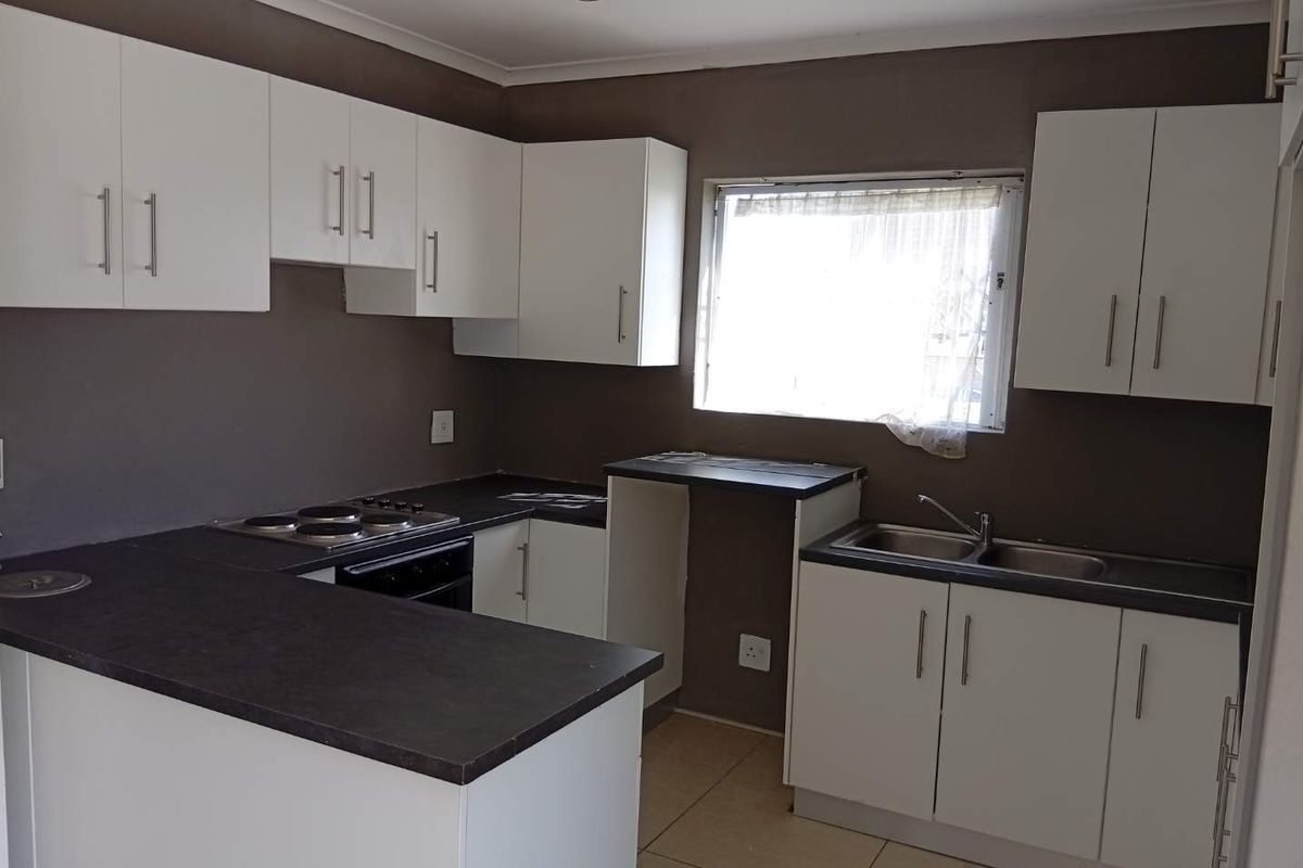 A functional kitchen featuring white cabinetry, dark countertops, a built-in oven and hob, and a double stainless steel sink with tiled flooring.