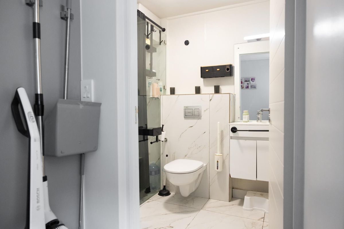 Modern bathroom featuring a wall-mounted toilet with concealed cistern, vanity cabinet with basin, and a glass-enclosed shower with marble-look tiling.