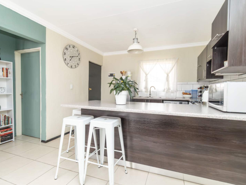 Open plan kitchen featuring a breakfast bar, dark wood cabinetry, laminate countertops, and tiled flooring, seamlessly connecting to the living area.