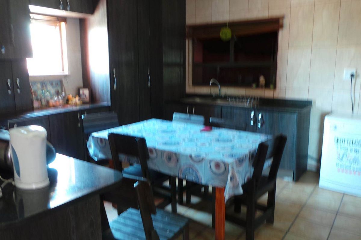 A functional kitchen featuring dark cabinetry, tiled walls, and a dedicated dining area with tiled flooring.