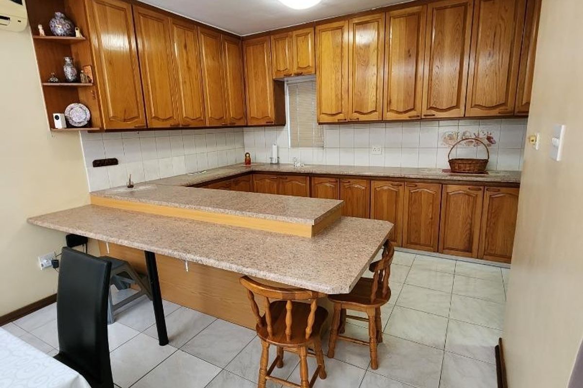 A functional kitchen featuring traditional wooden cabinetry, laminate countertops with an integrated breakfast bar, and tiled flooring throughout.