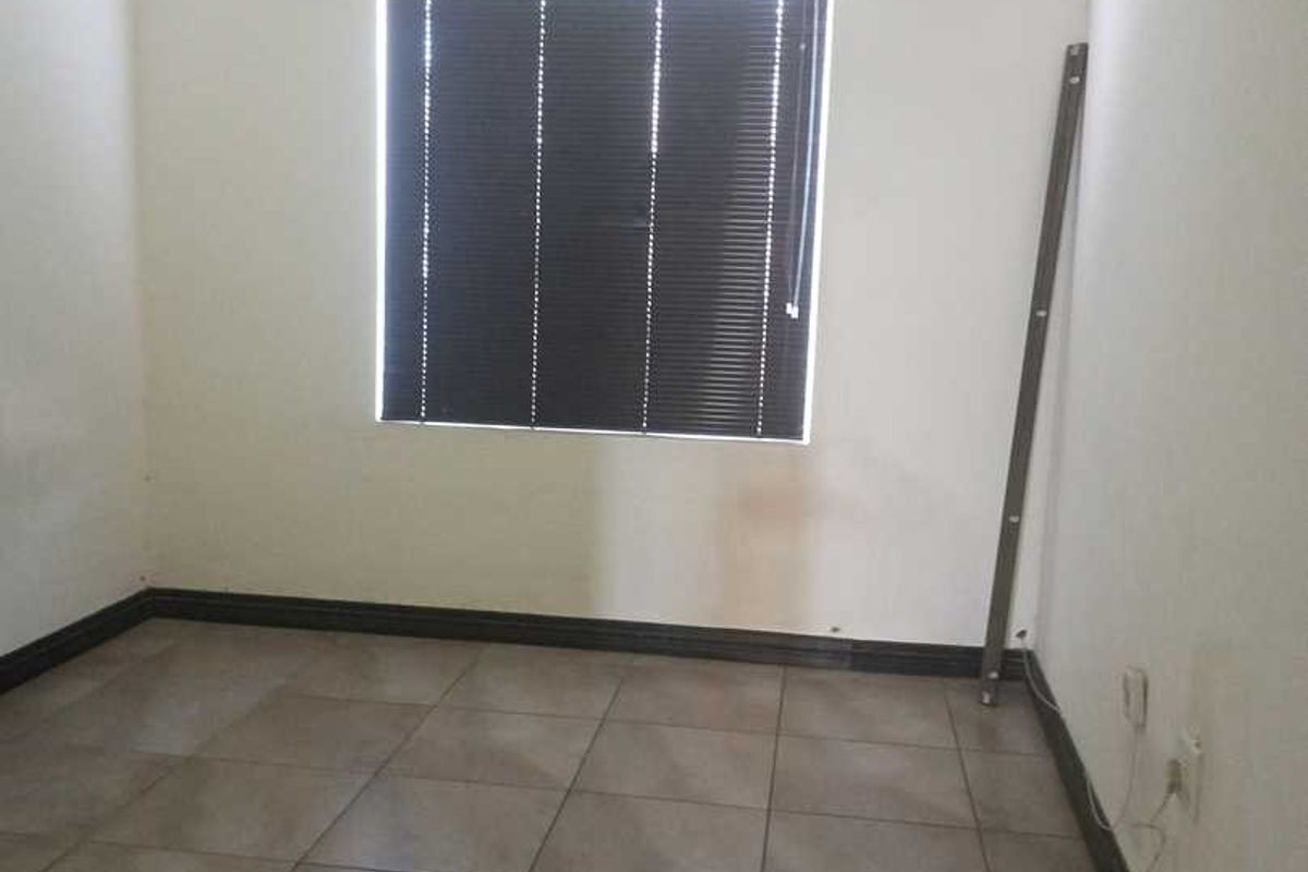 A vacant bedroom featuring neutral tiled flooring, a window with fitted blinds, and standard wall finishes.
