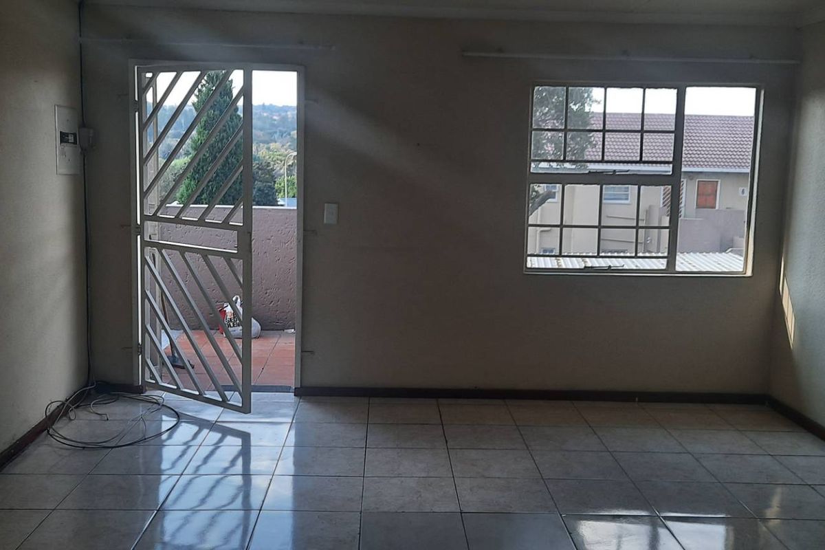 An empty living room featuring tiled flooring, a security gate leading to a balcony, and natural light through a window.
