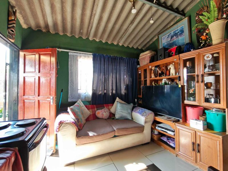 A living room featuring tiled flooring and an exposed corrugated roof structure, providing a functional space with potential for cosmetic updates.