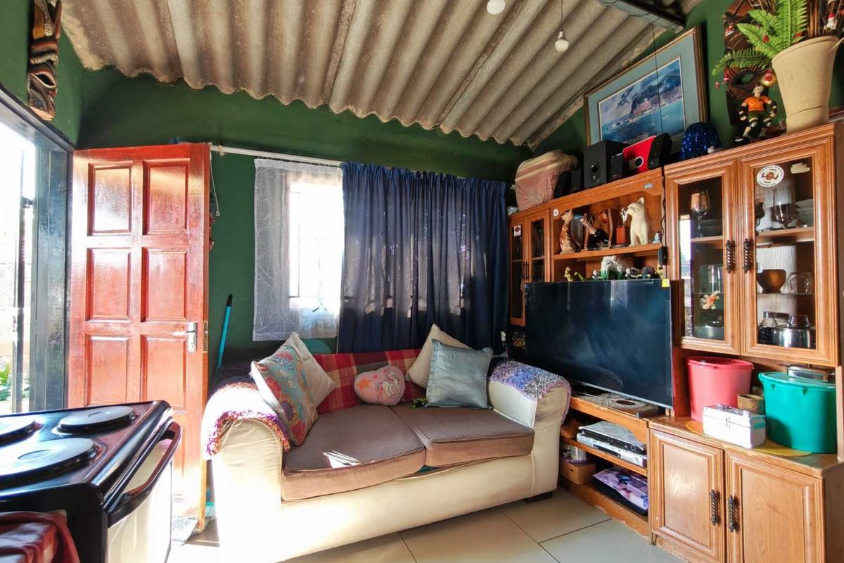 A living room featuring tiled flooring and an exposed corrugated roof structure, providing a functional space with potential for cosmetic updates.