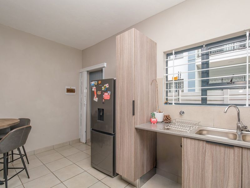 A functional kitchen area featuring modern wood-look cabinetry, a stainless steel sink, and tiled flooring, with security bars installed on the window.
