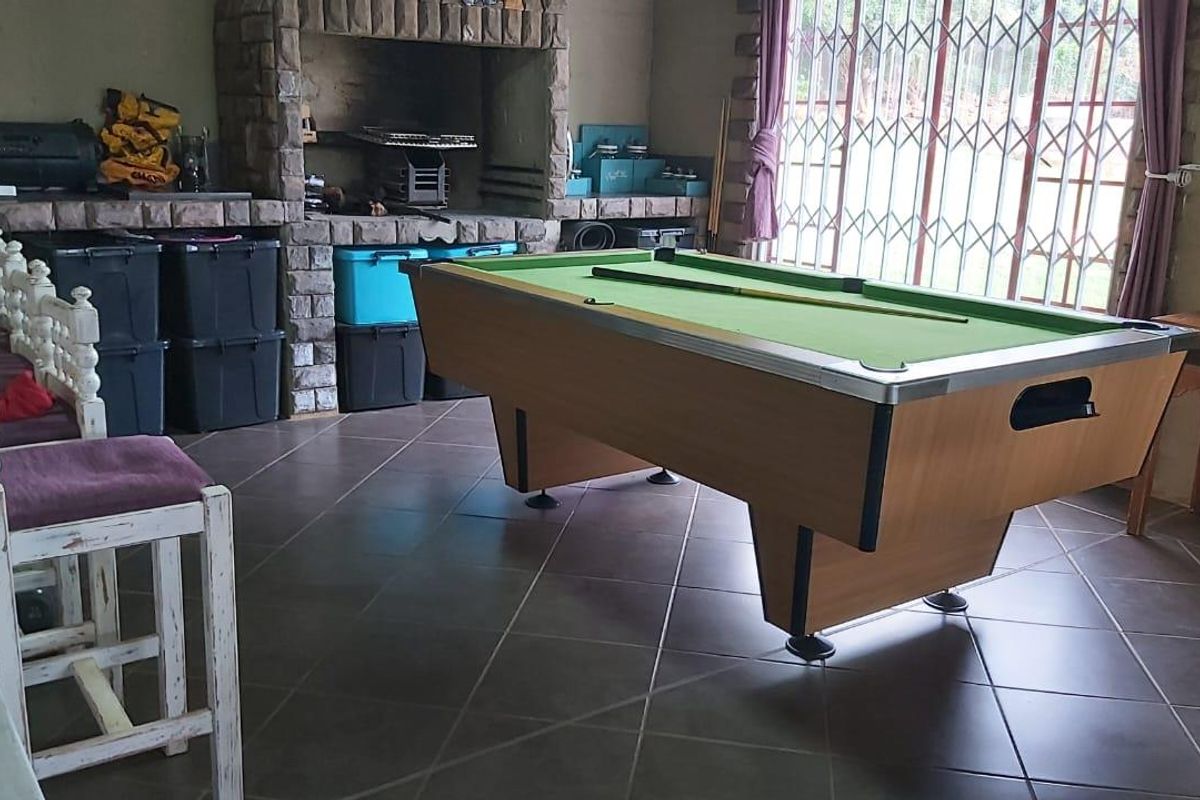 An indoor entertainment area featuring a built-in stone braai fireplace and tiled flooring, providing a functional space for social gatherings.