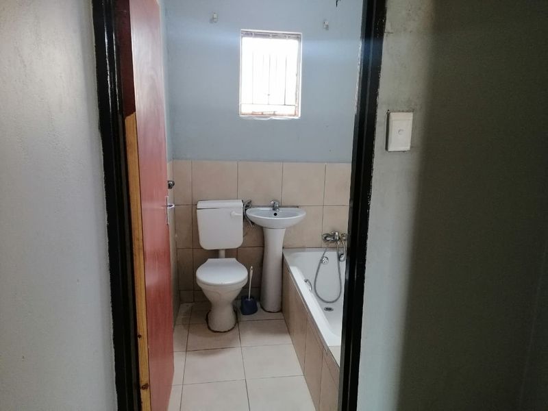 A compact bathroom featuring a pedestal basin, toilet, and bathtub with tiled finishes, requiring cosmetic updates to improve its overall condition.