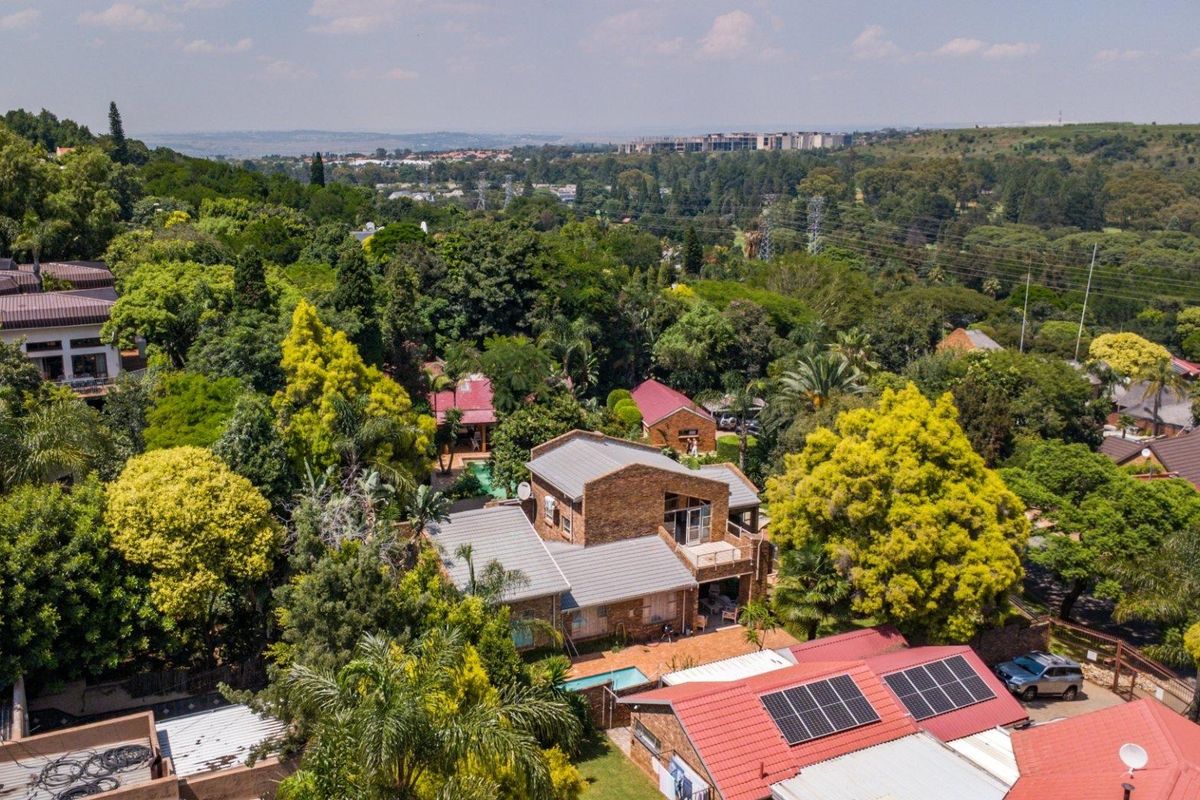 Aerial view of a residential property featuring a multi-level house with a tiled roof, surrounded by lush mature trees and established garden landscaping.