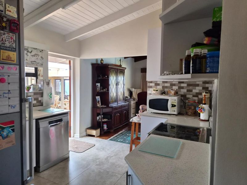 A functional kitchen featuring stone countertops, tiled backsplash, and exposed beam ceilings, with direct access to an outdoor patio area.