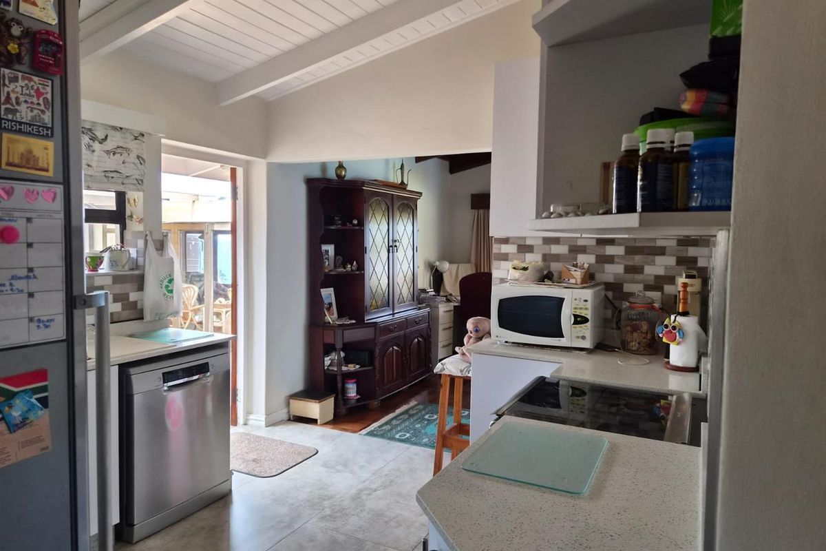 A functional kitchen featuring stone countertops, tiled backsplash, and exposed beam ceilings, with direct access to an outdoor patio area.