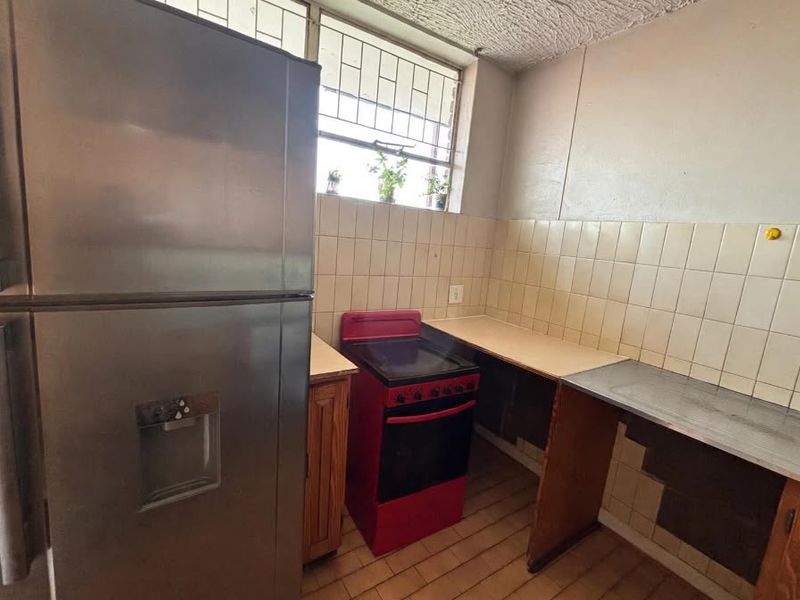 A functional kitchen featuring tiled backsplash, stainless steel sink, and built-in cabinetry, offering potential for modernization and cosmetic updates.