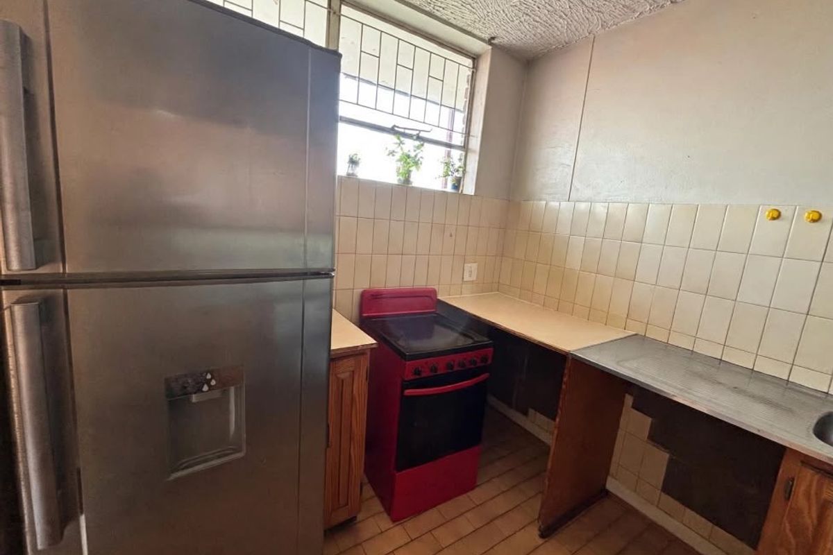 A functional kitchen featuring tiled backsplash, stainless steel sink, and built-in cabinetry, offering potential for modernization and cosmetic updates.