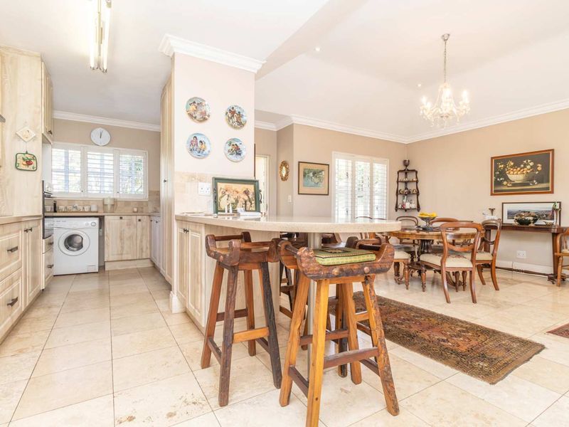 Spacious open-plan kitchen and dining area featuring light wood cabinetry, stone countertops, breakfast bar, and tiled flooring with elegant crown molding throughout.