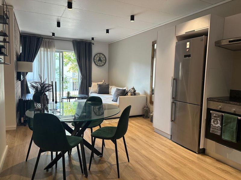 Modern open-plan living area featuring laminate flooring, integrated kitchen appliances, and a sliding door leading to a balcony.