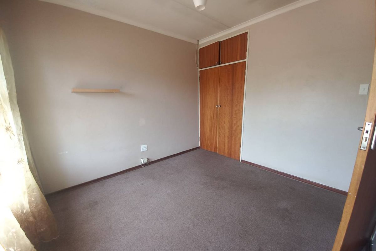 A bedroom featuring neutral walls, carpeted flooring, and built-in wooden cupboards with overhead storage compartments.