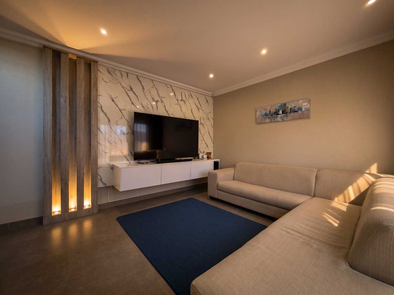 Modern living room featuring a marble-look feature wall, integrated timber slat paneling with accent lighting, and a sleek floating media console.